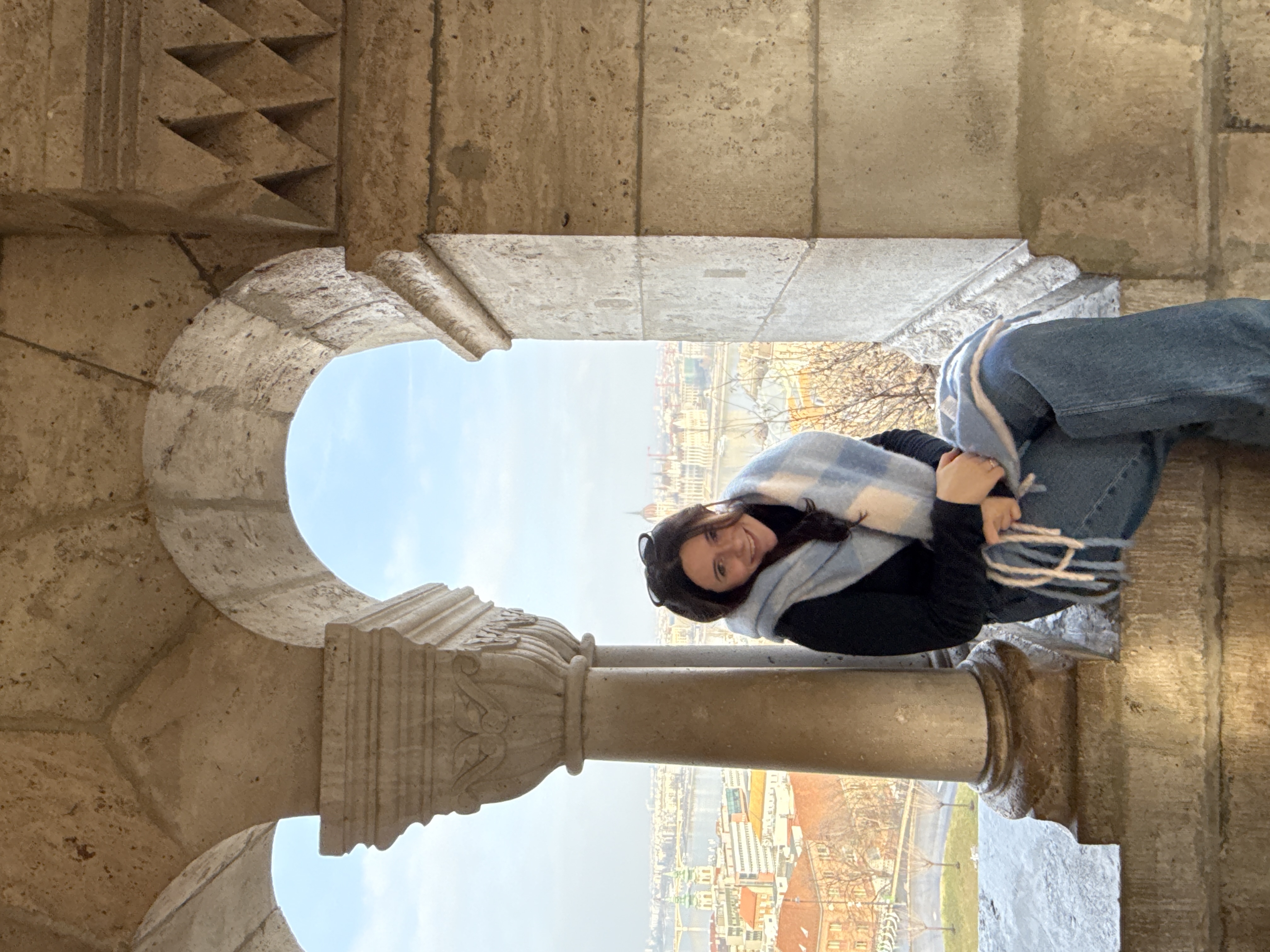 Person seated on a stone ledge within arches, overlooking a cityscape